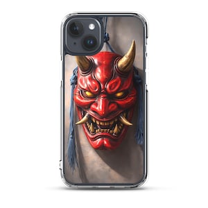 May include: A clear phone case featuring a graphic of a red Hannya mask with gold horns and glowing yellow eyes. The mask is adorned with blue tassels hanging from the sides, set against a neutral background, protecting a dual-lens smartphone.
