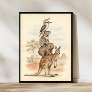 May include: A framed print featuring a whimsical illustration of Australian animals. A kangaroo supports a wombat, a koala, and a kookaburra, all stacked on top of each other. The background depicts a desert landscape with a red dirt path and a mesa.