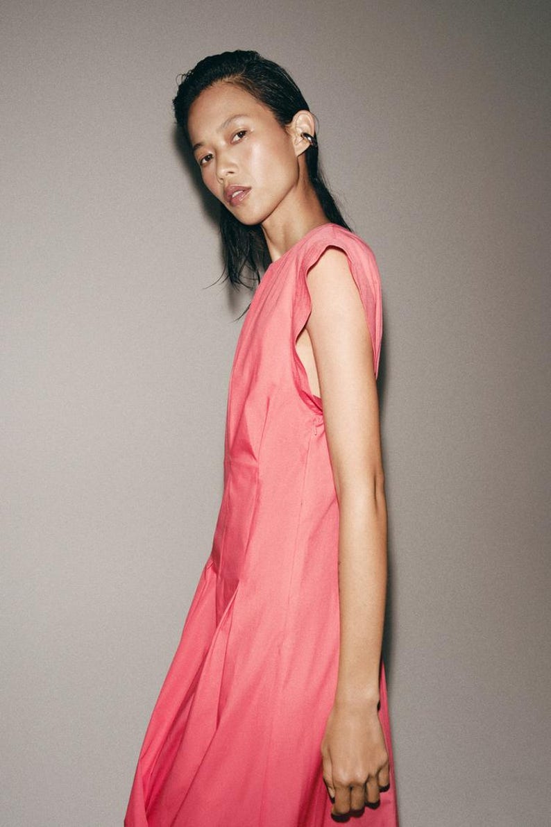 May include: A sleeveless dress in a vibrant shade of pink, featuring a round neckline and structured shoulder detailing. The garment is crafted from a smooth, solid-colored fabric that falls in a clean, straight silhouette along the body.