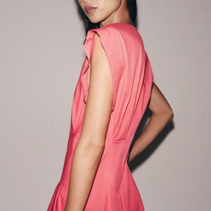 May include: A vibrant pink sleeveless dress featuring structured shoulder details with subtle pleating. The garment has a fitted bodice that transitions into a flared skirt, showcasing a clean, solid color design with a smooth, matte fabric finish.