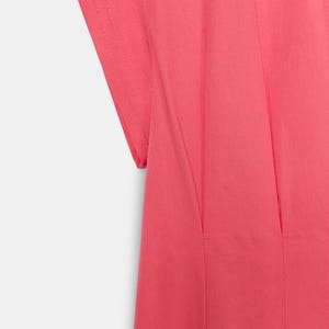 May include: A bright pink garment featuring short sleeves with visible stitched detailing along the edges. The fabric displays vertical pleats or seams that run downward from the shoulder area, creating a structured and clean appearance.