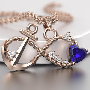 Pode incluir: Colar com pingente em ouro rosa com uma âncora e um símbolo de infinito, adornado com uma pedra preciosa azul em forma de coração e pequenas pedras preciosas brancas. O colar é exibido em uma superfície branca.