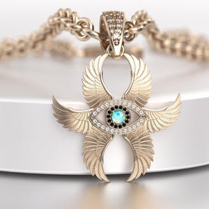 May include: Gold-toned pendant necklace featuring an Ankh symbol with stylized wings and an eye design. The eye has a central blue-green stone surrounded by black and clear stones. The chain is a thick, textured gold. Jewelry.