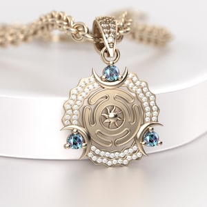 May include: Gold-toned pendant necklace featuring a circular design with a sunburst center and crescent moon accents. The pendant is adorned with small, sparkling gemstones and three blue-green stones. The necklace chain is also gold-toned.