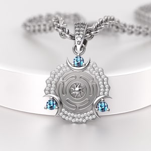 May include: Silver pendant necklace featuring a circular design with a sunburst center and a maze pattern. The pendant is adorned with blue gemstones and small clear stones. The necklace has a silver chain.