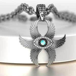 May include: A silver-colored pendant necklace featuring an Ankh symbol with stylized wings. The pendant has an eye design with a central blue-green stone, surrounded by clear and black gemstones. The chain is a thick, textured silver.