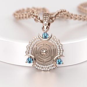 May include: Rose gold pendant necklace featuring a circular pendant with a sunburst design at the center, surrounded by a diamond-studded border. The pendant has three blue gemstones and crescent moon accents. The necklace chain is also rose gold.