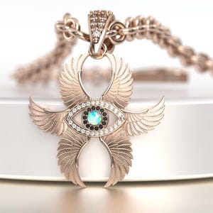 May include: Rose gold pendant necklace featuring an eye-shaped design with feathered wings. The pendant has a central opal-like stone, surrounded by white and black gemstones. The chain is also rose gold.
