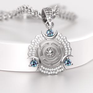 May include: Silver pendant necklace featuring a circular pendant with a sunburst design at the center. The pendant has three crescent moon accents, each with a blue gemstone. The necklace is on a silver chain.