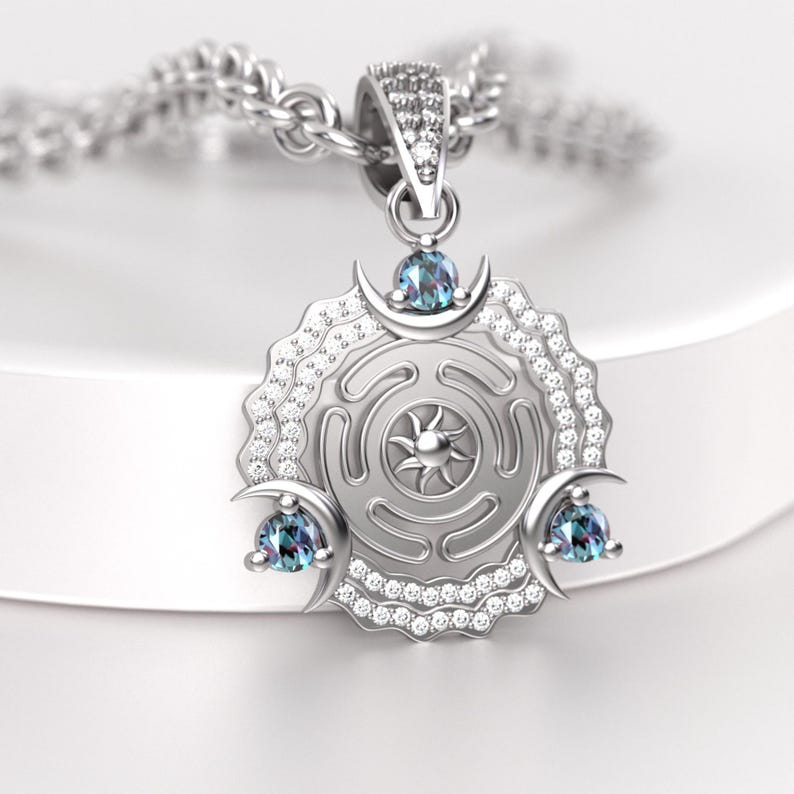 May include: Silver pendant necklace featuring a circular pendant with a sunburst design at the center. The pendant has three crescent moon accents, each with a blue gemstone. The necklace is on a silver chain.
