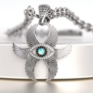 May include: A silver pendant necklace featuring a stylized eye design with feathered wings. The eye has a blue center and is surrounded by clear crystals and a black border. The pendant hangs from a silver chain.