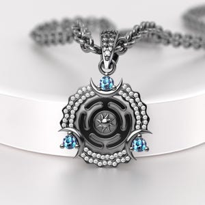 May include: A silver pendant necklace featuring a circular design with a sunburst center and three blue gemstones. The pendant is adorned with small, clear crystals and crescent moon accents. The necklace chain is also silver.