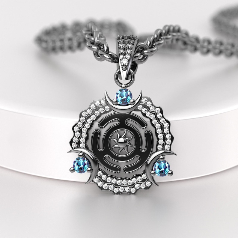 May include: A silver pendant necklace featuring a circular design with a sunburst center and three blue gemstones. The pendant is adorned with small, clear crystals and crescent moon accents. The necklace chain is also silver.