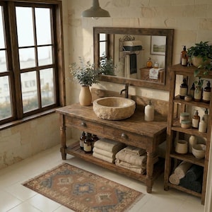 Puede incluir: Un baño rústico con un mueble de tocador de madera, un lavabo de piedra y un espejo grande. El tocador tiene cajones y un estante inferior con toallas dobladas. Una estantería de madera contiene artículos de tocador. Una alfombra estampada está en el suelo embaldosado.