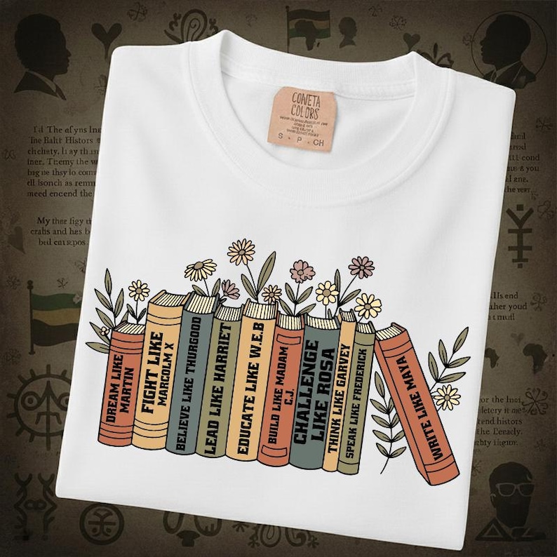 May include: White t-shirt with a graphic of books and flowers. The books have titles like "Dream Like Martin" and "Write Like Maya". A small tag on the shirt reads "CONETA COLORS".