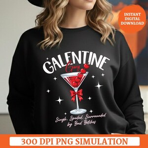 Puede incluir: Sudadera negra con el texto "GALENTINE Gang" en blanco y rojo. Se muestra una copa de cóctel con cerezas y un lazo rojo. El texto "Single, Spoiled, Surrounded by Bad Bitches" está debajo.