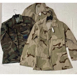 Könnte beinhalten: Eine weiße Keramik-Tasse mit schwarzem Henkel und dem Text "But First, Coffee" in fetter, schwarzer Schrift. Die Tasse steht vor einem verschwommenen Hintergrund. Die Tasse ist etwa 10 cm hoch.