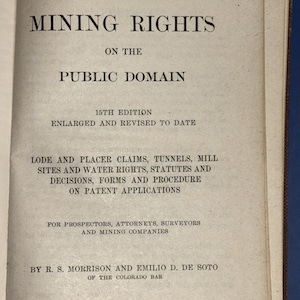 May include: An open book with the title "MINING RIGHTS" in large, bold, black letters. The text continues with "ON THE PUBLIC DOMAIN" and further details about mining claims, statutes, and patent applications. The book is a 15th edition, enlarged and revised.