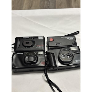 以下が含まれることがあります： 4台の黒いポイントアンドシュートフィルムカメラが表示されています。2台はKeystoneブランド、1台はVivitar、1台はVivitar Point 'N Shootです。Keystoneカメラには「455 Panorama」と「Auto Flash Red Eye Reduction」の文字があります。