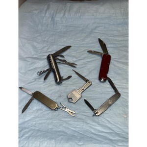 May include: An assortment of multi-tools and pocket knives, including a silver multi-tool with a corkscrew, a red-handled knife, and a key-shaped tool. Blades and tools are open, showcasing their functionality.
