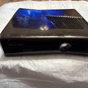 Peut inclure: Une console Xbox 360 noire avec une finition brillante. La console comprend un lecteur de disque, un bouton d'alimentation et le logo Xbox 360. Le dessus de la console présente une conception d'aération.