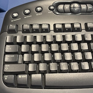 May include: A close-up of a black computer keyboard with white lettering. The keyboard has function keys, number keys, and letter keys. There are also multimedia control buttons. The keyboard is designed for ease of use and efficiency.