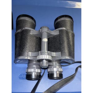 May include: Black and gray binoculars with a textured grip. The binoculars have adjustable focus rings and a black strap. The lenses are black and the body is gray. The binoculars are designed for viewing distant objects.