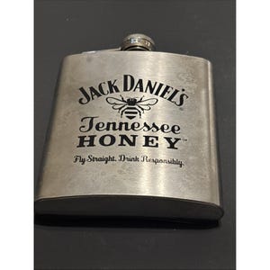 May include: A stainless steel flask with a screw-on cap. The flask features the "Jack Daniel's Tennessee HONEY" logo with a bee graphic and the text "Fly Straight, Drink Responsibly."
