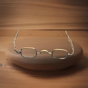 May include: A pair of eyeglasses featuring thin, metallic frames with a textured, wavy design on the temples. The rectangular lenses are framed by a silver-toned metal with subtle gold-toned accents along the top edges of the rims.