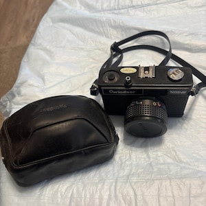 May include: A black Windsor W233-GF camera with a lens cap and a black leather case. The camera has a black strap and a silver flash. The lens is black with a yellow, red, and green color ring.