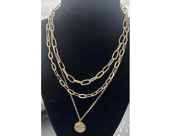 Collar de varias capas en tono dorado con colgante de moneda y cadena tipo clip.