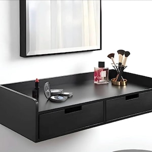 Puede incluir: Un tocador flotante negro con dos cajones, un espejo y accesorios de maquillaje. El tocador tiene un diseño moderno. Los accesorios incluyen lápiz labial, sombra de ojos, perfume y brochas de maquillaje.