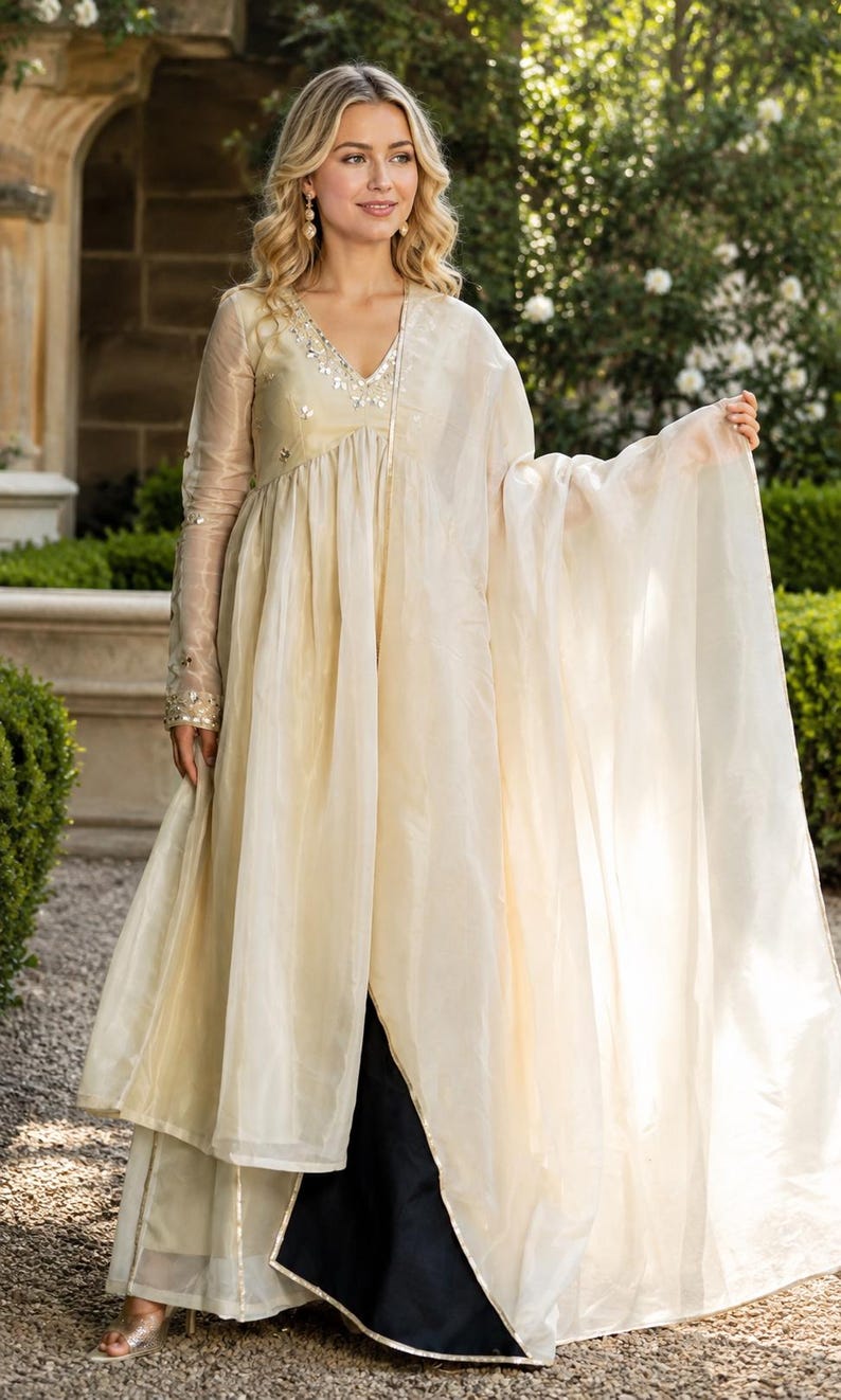 May include: A cream-colored long-sleeved tunic with a V-neckline featuring silver mirror embellishments, paired with a matching sheer dupatta and dark trousers. The tunic has a flowing silhouette with a central front slit and sheer sleeves.
