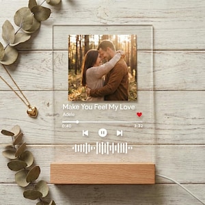 Może przedstawiać: Przezroczysta akrylowa tablica ze zdjęciem pary, tytułem piosenki "Make You Feel My Love" Adele i graficznym przedstawieniem fali dźwiękowej. Zamontowana na drewnianej podstawie, z białym kablem.