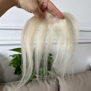 May include: A hair topper piece featuring straight, platinum blonde hair strands attached to a small, circular base. The hair is fine in texture and light in color, designed to provide coverage or added volume to the top of the head.