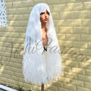 May include: A long, wavy white wig with bangs is displayed on a mannequin head. The wig has a natural-looking texture and falls past the shoulders. The mannequin is positioned in front of a light-colored brick wall.