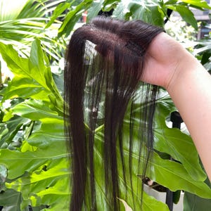 Op de afbeelding: Een donkerbruin haartoevoeging met een fijne mesh basis en geïntegreerde clips voor bevestiging. Het haar is steil, glad en lang met een natuurlijke glans. De constructie bevat een zichtbare scheiding die is ontworpen om met eigen haar te mengen.