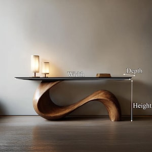 May include: A contemporary console table featuring a dark, rectangular top and a distinctive, flowing wooden base. Two small, cylindrical lamps with cream shades are placed on the table. A small, rectangular book is also on the table.