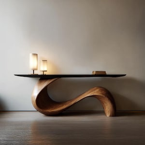 May include: A contemporary wooden console table with a distinctive, curved design. The table has a dark, rectangular top and a sculptural base crafted from light brown wood. Two small lamps with cylindrical shades are on the table, and a small book rests on the right side.