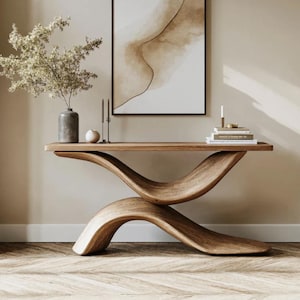 May include: A contemporary wooden console table with a distinctive, curved form. The table is crafted from light brown wood and has a long, rectangular top supported by two intersecting, wave-shaped structures. Decorative items, including a vase with flowers, candles, and books, are placed on the table.