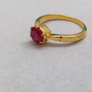 May include: A gold ring with a vibrant red gemstone. The ring features a classic design with a round, faceted ruby set in a gold band. The band has a simple, elegant design, making it a timeless piece of jewelry.