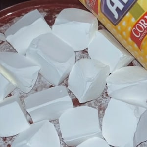 Puede incluir: Primer plano de bloques blancos de forma irregular, posiblemente tiza, dispersos sobre una superficie roja. Un recipiente amarillo de maicena Argo es parcialmente visible, con el texto "sin gluten".