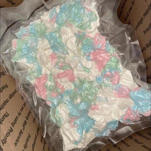 Puede incluir: Un paquete que contiene un artículo sellado al vacío con una combinación de colores pastel rosa, azul y verde. El artículo está dentro de una caja de cartón con el texto "Priority Mail" y "Thank you" visible.