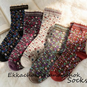 Könnte beinhalten: Eine Auswahl an Socken mit Blumenmuster in verschiedenen Farben, darunter Schwarz, Burgunderrot, Creme und Dunkelrot. Jede Socke hat eine zarte Spitzenborte am oberen Rand. Der Text "Ekkachai Sirichok Socks" ist unten aufgedruckt.