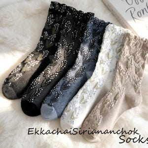 May include: Five pairs of floral patterned socks in various colors: black, charcoal, blue, white, and beige. The socks have a delicate, embroidered floral design. The brand name "EkkachaiSiriananchok Socks" is printed at the bottom.