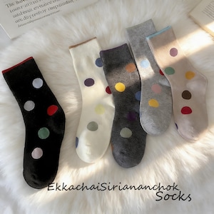 May include: Five pairs of crew socks featuring a polka dot pattern in various colors. The socks come in black, cream, dark gray, light gray, and beige, each with a contrasting colored cuff and multicolored circular dots scattered across the fabric.