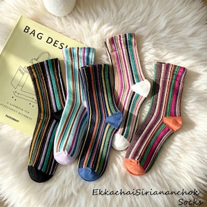 May include: Five pairs of crew socks featuring vertical stripes in various color combinations including black, green, blue, orange, and purple. Each sock has a solid colored heel and toe section. The socks are arranged in a fan pattern.