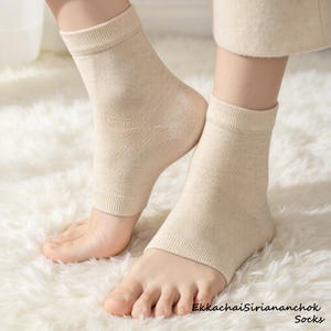 May include: A pair of beige ankle socks featuring a ribbed cuff and an open-toe design that exposes the toes. The fabric has a fine knit texture. The text EkkachaiSiriananchok Socks is printed in the bottom right corner of the image.