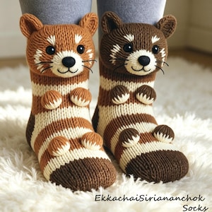 May include: A pair of knitted socks featuring red panda designs. The socks have brown, cream, and white stripes, with 3D paws and red panda faces. The text "EkkachaiSiriananchok Socks" is visible at the bottom.