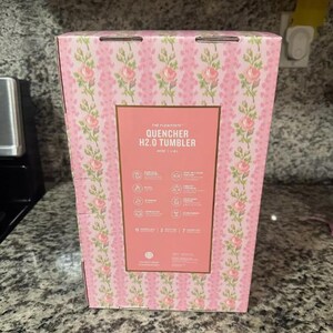 May include: A pink box with a floral pattern and the text "THE FLOW STATE QUENCHER H2.0 TUMBLER" in white. The box has a rectangular label with icons and text describing the product's features. The box is 11 inches tall.